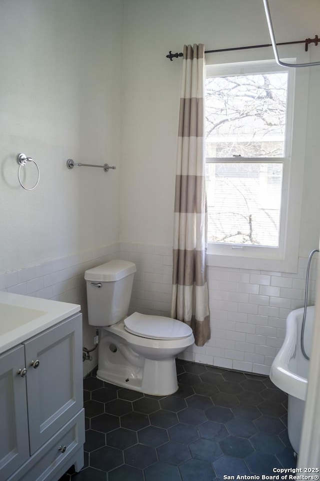 full bathroom with tile patterned flooring, a healthy amount of sunlight, tile walls, and wainscoting