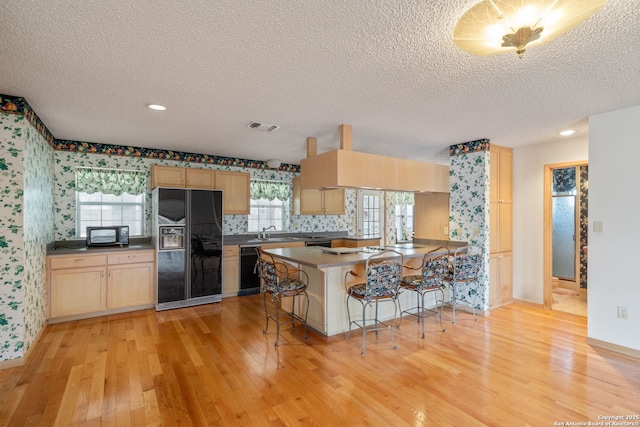 831 Hill Top, Canyon Lake, TX 78133 - kitchen with visible vents, a peninsula, wallpapered walls, black appliances, and light brown cabinetry