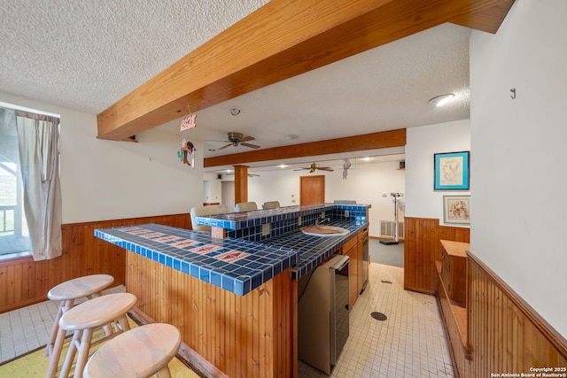 831 Hill Top, Canyon Lake, TX 78133 - kitchen featuring tile counters, wooden walls, beam ceiling, and a wainscoted wall