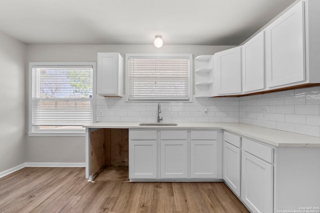 kitchen featuring white cabinetry, light countertops, backsplash, a sink, and light wood-style floors