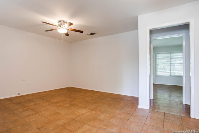 unfurnished room with a ceiling fan, visible vents, and baseboards