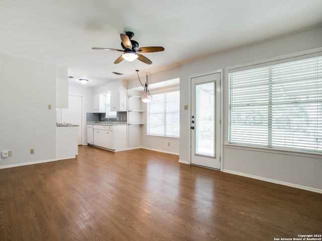 unfurnished living room with a sink, a ceiling fan, visible vents, baseboards, and wood finished floors