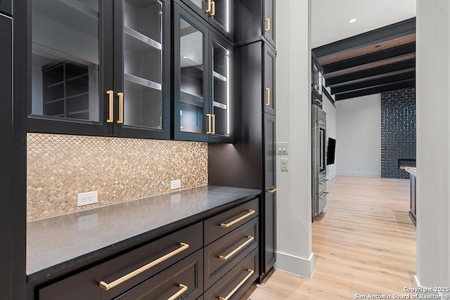 kitchen featuring tasteful backsplash, baseboards, light wood-style floors, glass insert cabinets, and a stone fireplace