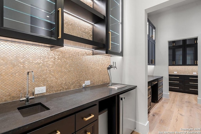 kitchen with a sink, decorative backsplash, glass insert cabinets, light wood-type flooring, and high quality fridge