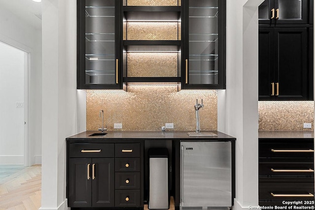 bar with a sink, indoor wet bar, backsplash, baseboards, and freestanding refrigerator