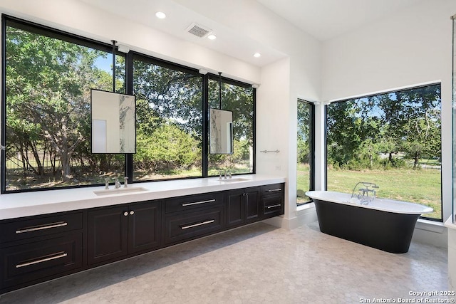 full bathroom with a sink, a freestanding tub, double vanity, visible vents, and recessed lighting