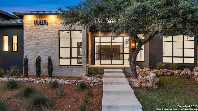 view of exterior entry with stone siding, a standing seam roof, metal roof, and stucco siding