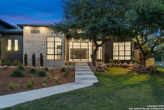 contemporary house with a standing seam roof, stone siding, metal roof, and a front yard