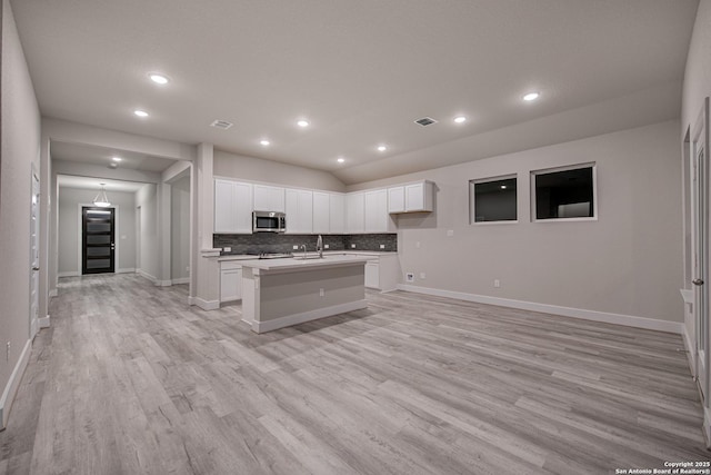 9331 Pioneer Jct, San Antonio, TX 78254 - kitchen featuring stainless steel microwave, a kitchen island with sink, light wood-style floors, backsplash, and white cabinetry
