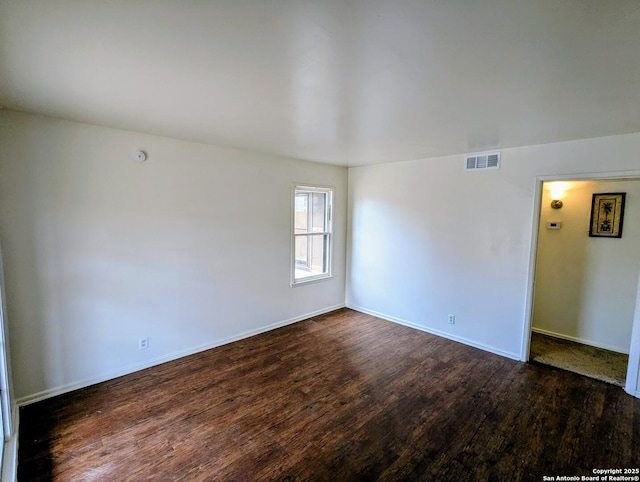 empty room with dark wood-style floors, visible vents, and baseboards