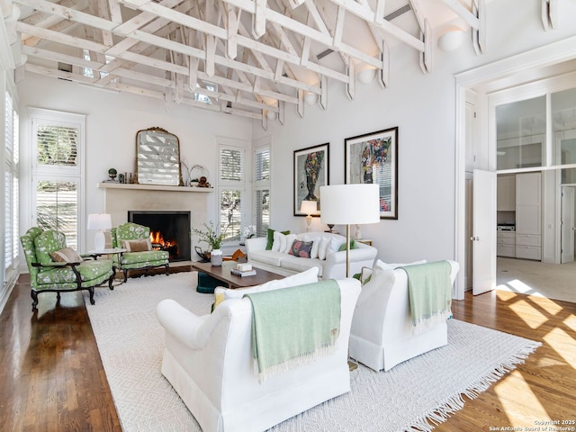living area featuring high vaulted ceiling, beam ceiling, a warm lit fireplace, and wood finished floors