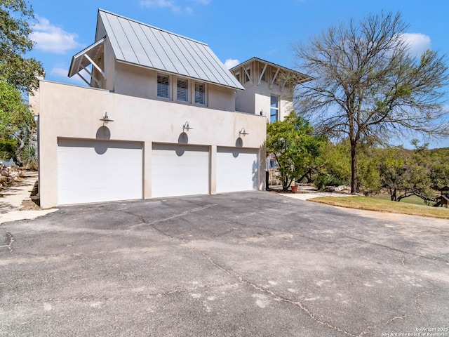 view of home's exterior featuring aphalt driveway, a garage, stucco siding, a standing seam roof, and metal roof
