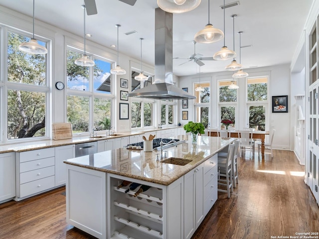 kitchen featuring ceiling fan, stainless steel appliances, island range hood, dark wood-type flooring, and a center island with sink