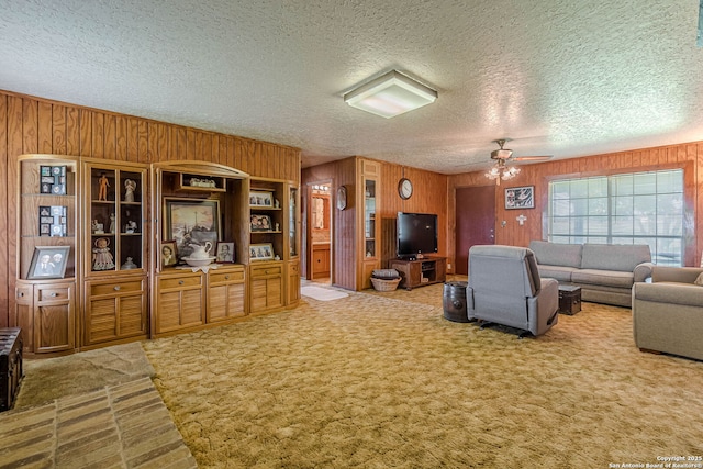 carpeted living area with a textured ceiling, wood walls, and a ceiling fan