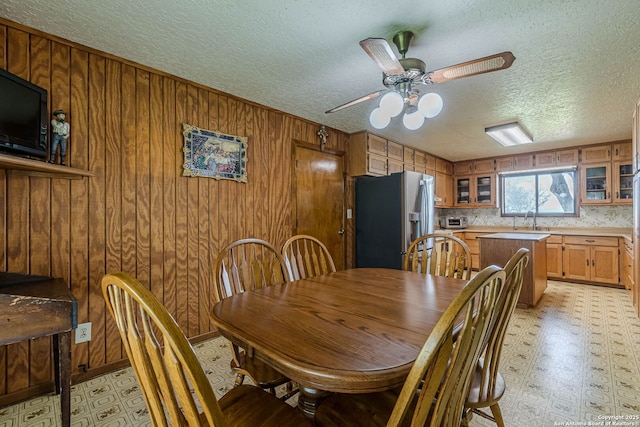 dining area featuring ceiling fan, wood walls, light floors, and a textured ceiling
