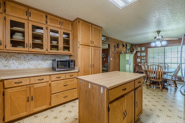 kitchen with a ceiling fan, light floors, a textured ceiling, a center island, and stainless steel microwave