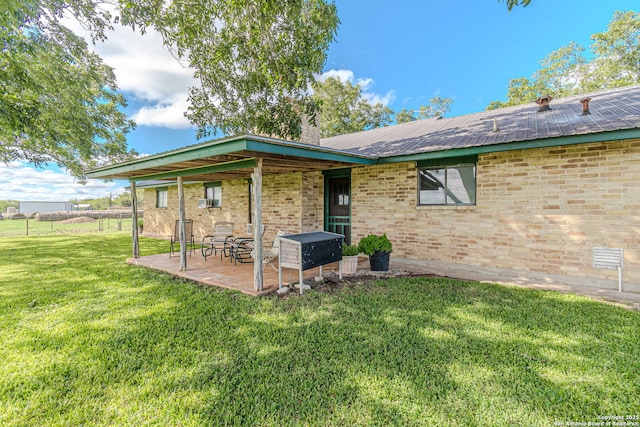 back of house with a lawn, metal roof, a patio area, and brick siding