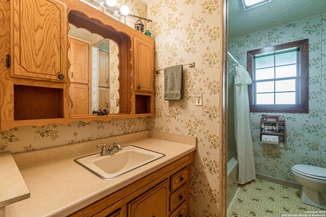 full bathroom featuring wallpapered walls, vanity, toilet, and a textured ceiling