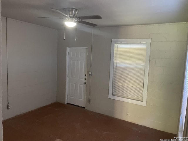 empty room featuring concrete flooring, concrete block wall, and a ceiling fan