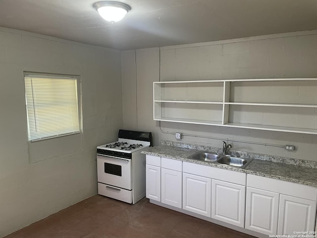 kitchen featuring white cabinets, white gas range, concrete block wall, a sink, and open shelves