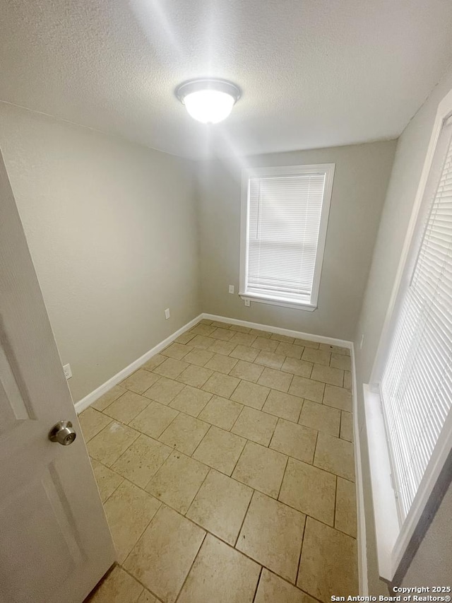 unfurnished room with baseboards and a textured ceiling