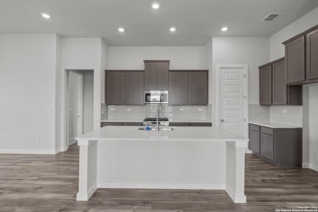 1509 Passmore Downs, New Braunfels, TX 78130 - kitchen with stainless steel microwave, an island with sink, tasteful backsplash, wood finished floors, and recessed lighting