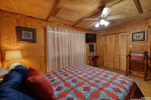 bedroom featuring wood walls, wood finished floors, visible vents, a closet, and ceiling fan