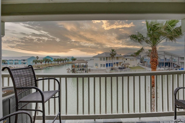 balcony at dusk featuring a residential view and a water view