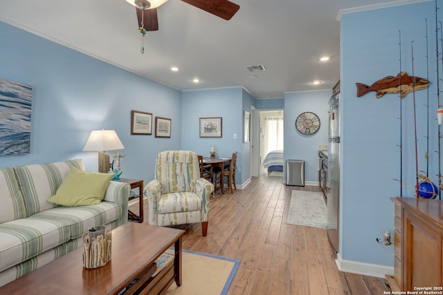 living area featuring light wood-type flooring, baseboards, visible vents, ceiling fan, and ornamental molding