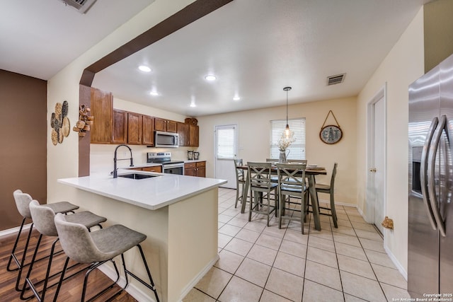 kitchen with light countertops, a sink, a breakfast bar, stainless steel appliances, and visible vents