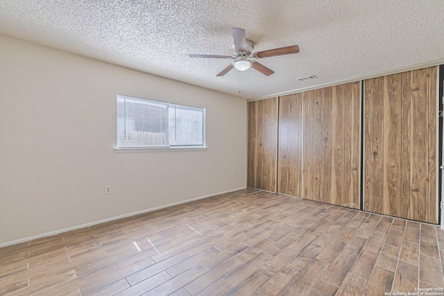 spare room featuring a textured ceiling, visible vents, baseboards, ceiling fan, and wood finished floors