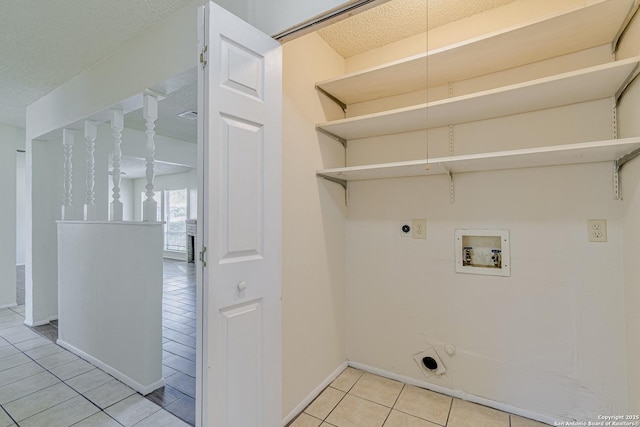 clothes washing area with electric dryer hookup, laundry area, light tile patterned floors, baseboards, and hookup for a washing machine