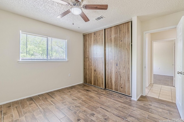unfurnished bedroom featuring wood finished floors, a textured ceiling, a closet, and visible vents
