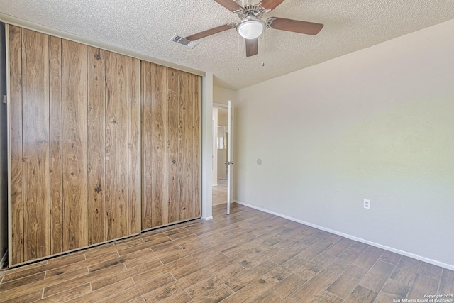 spare room featuring a textured ceiling, visible vents, baseboards, ceiling fan, and wood finished floors