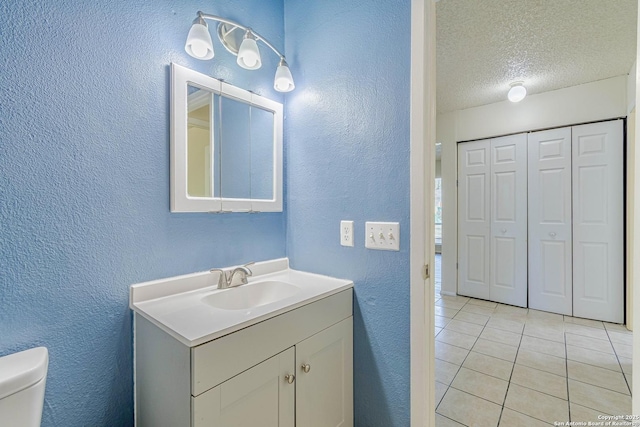 bathroom with tile patterned flooring, vanity, toilet, a textured wall, and a textured ceiling