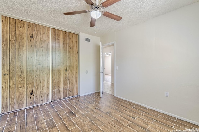 unfurnished room with a textured ceiling, ceiling fan, visible vents, and wood finished floors