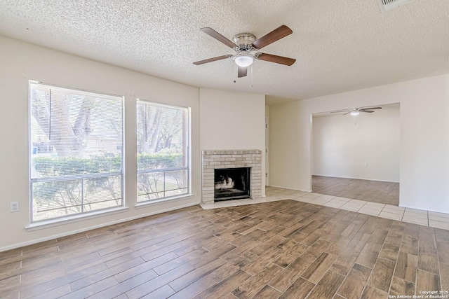 unfurnished living room with a brick fireplace, wood tiled floor, a textured ceiling, and a ceiling fan