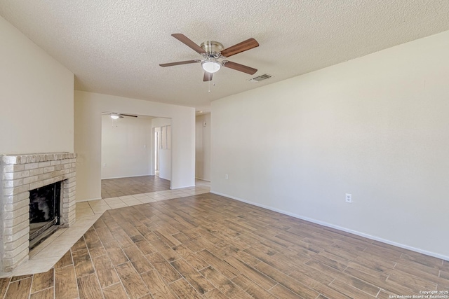 unfurnished living room with a textured ceiling, ceiling fan, wood finished floors, and a brick fireplace