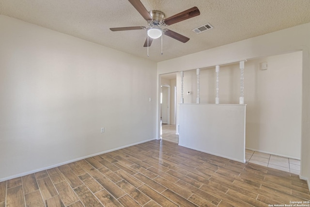empty room featuring wood finished floors, a textured ceiling, baseboards, visible vents, and ceiling fan
