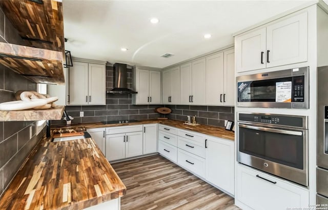 kitchen with butcher block countertops, decorative backsplash, and wall chimney exhaust hood