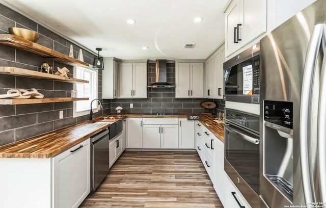 kitchen with stainless steel appliances, backsplash, wooden counters, a sink, and wall chimney range hood