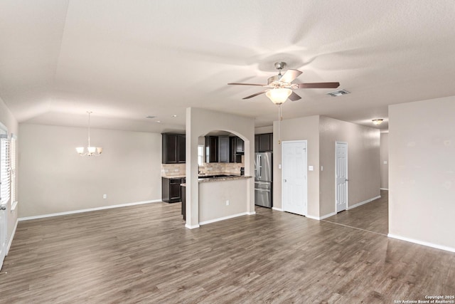 unfurnished living room with ceiling fan with notable chandelier, visible vents, wood finished floors, and baseboards