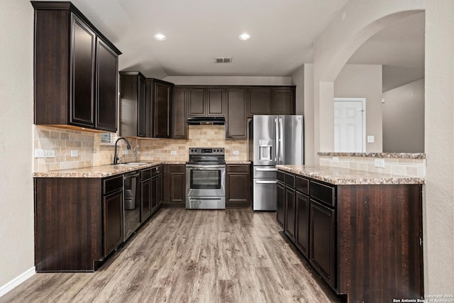 kitchen featuring a sink, appliances with stainless steel finishes, under cabinet range hood, visible vents, and arched walkways