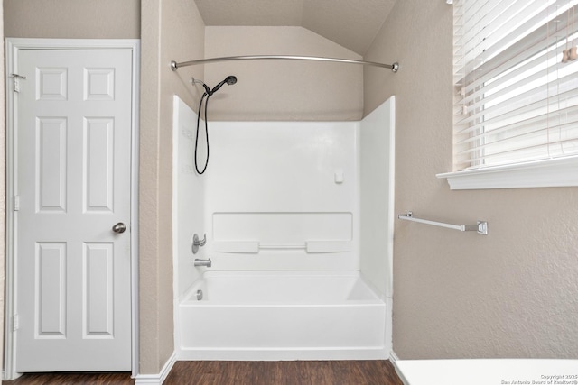 bathroom featuring baseboards, lofted ceiling, wood finished floors, and shower / bathtub combination