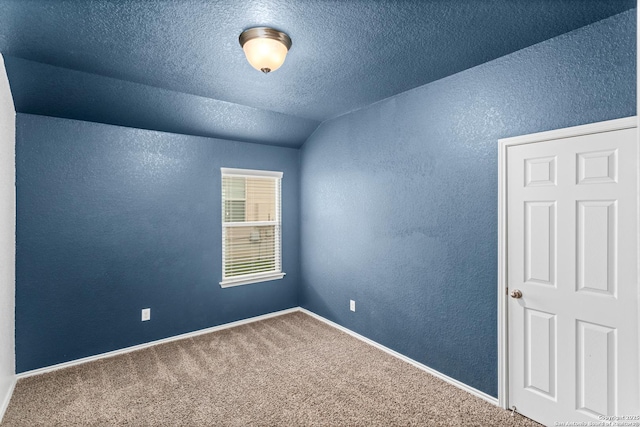 empty room with lofted ceiling, a textured ceiling, a textured wall, and carpet