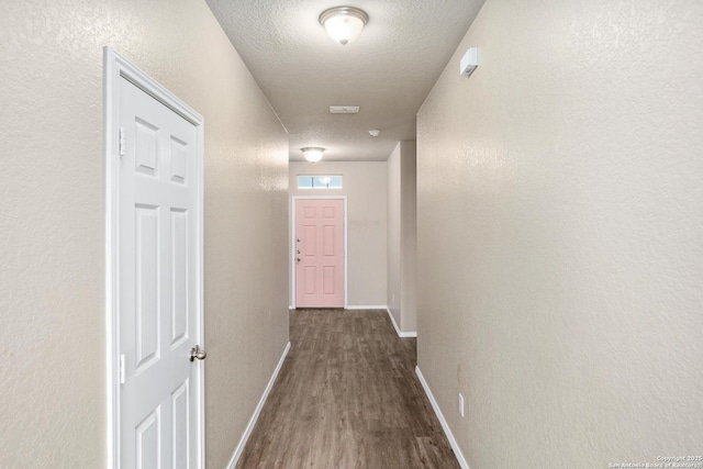 corridor with baseboards, dark wood-style flooring, a textured wall, and a textured ceiling