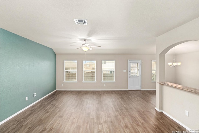 unfurnished living room with ceiling fan with notable chandelier, baseboards, arched walkways, visible vents, and wood finished floors