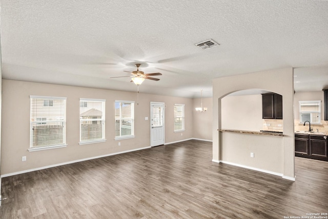unfurnished living room featuring visible vents, ceiling fan with notable chandelier, a healthy amount of sunlight, and dark wood finished floors