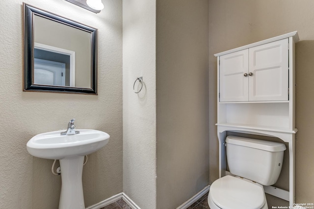 half bathroom featuring toilet, a textured wall, and baseboards