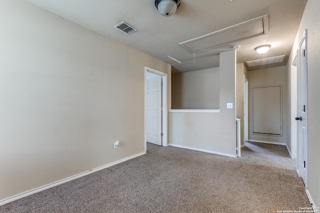 carpeted empty room featuring baseboards, attic access, and visible vents